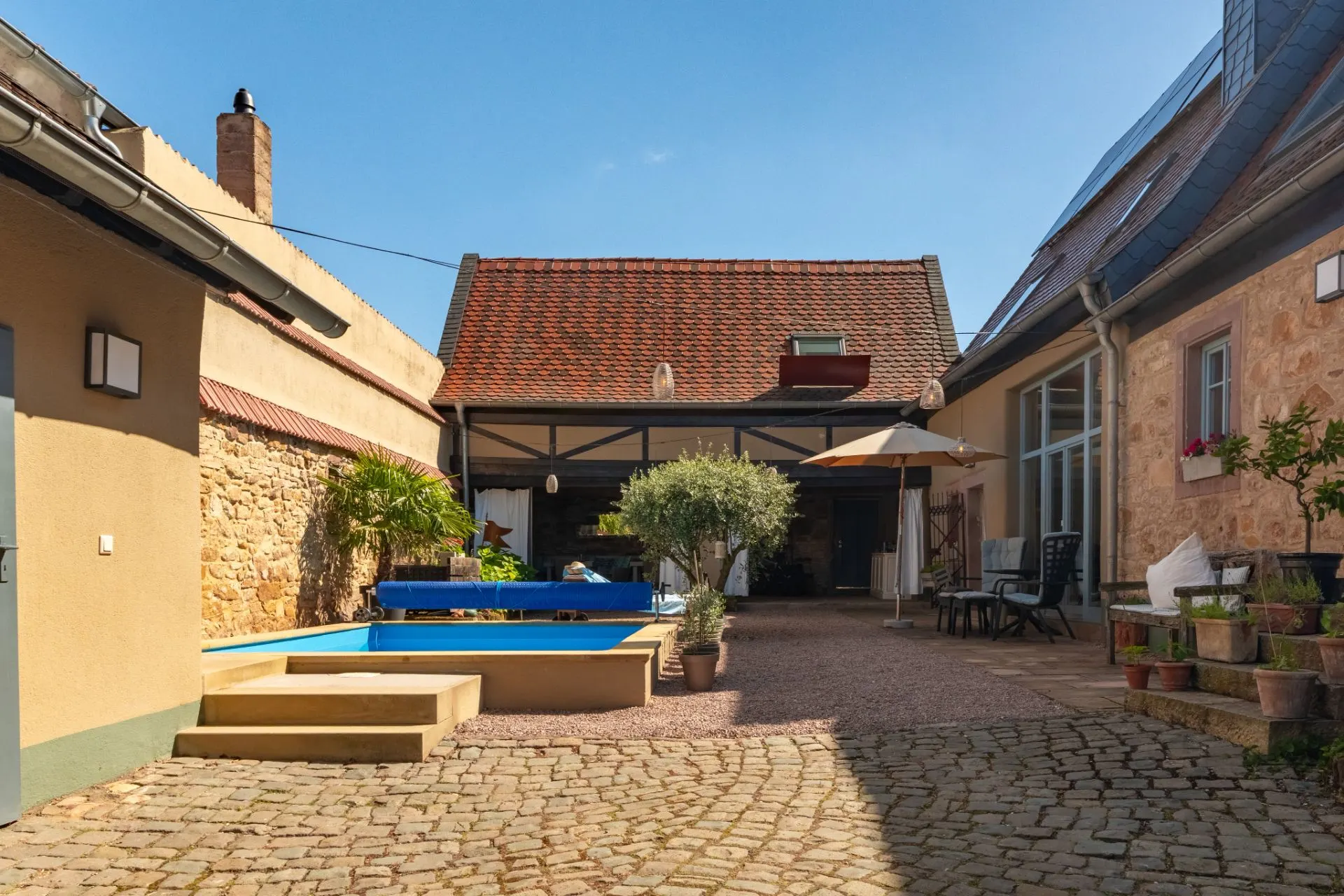 Innenhof mit kleinem Pool, Pflastersteinen, Pflanzen und Sitzbereich unter Sonnenschirm.