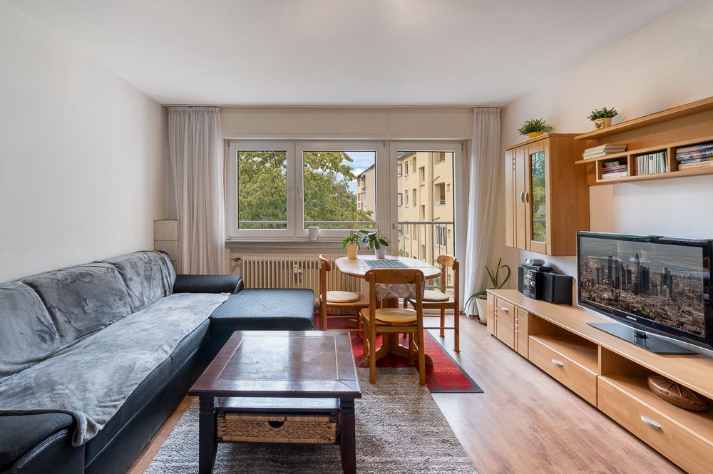 Wohnzimmer mit Sofa, Couchtisch, Essecke, Fernseher und großem Fenster mit Blick nach draußen.