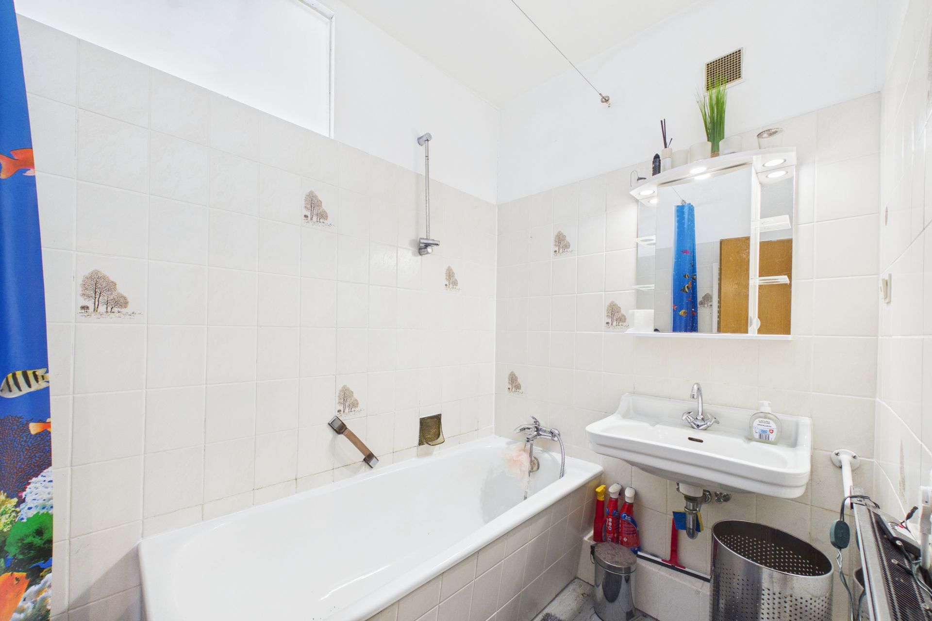 Helles Badezimmer mit Badewanne, Waschbecken, Spiegel und Duschvorhang mit Fischmotiv.