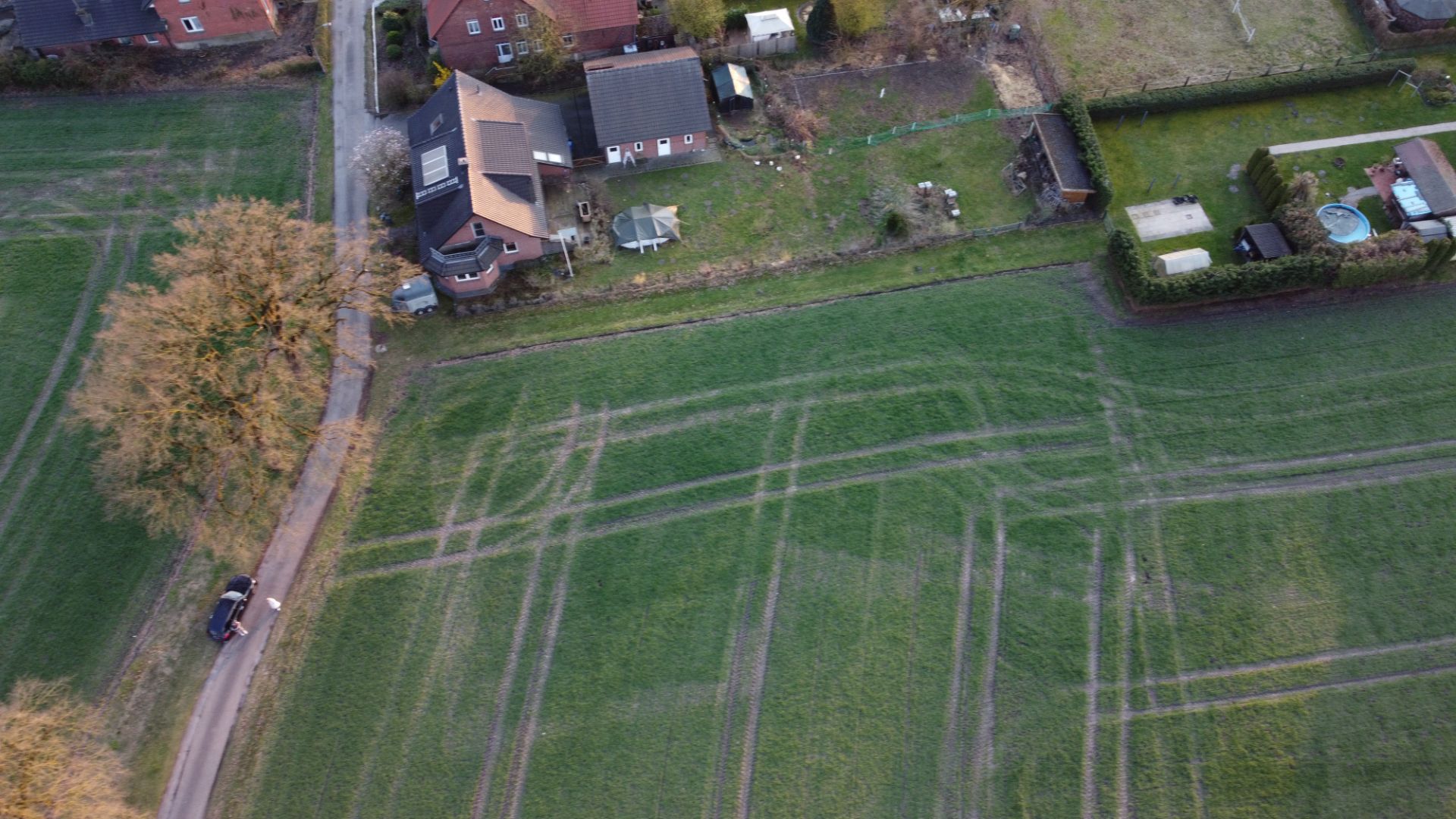 Luftaufnahme von Häusern mit Gärten, Feldern und einer schmalen Straße mit einem Auto.