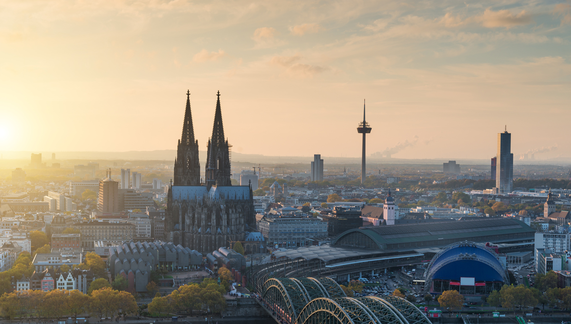 Stadtpanorama mit einem großen Dom, Bahnhof und Brücke bei Sonnenuntergang.