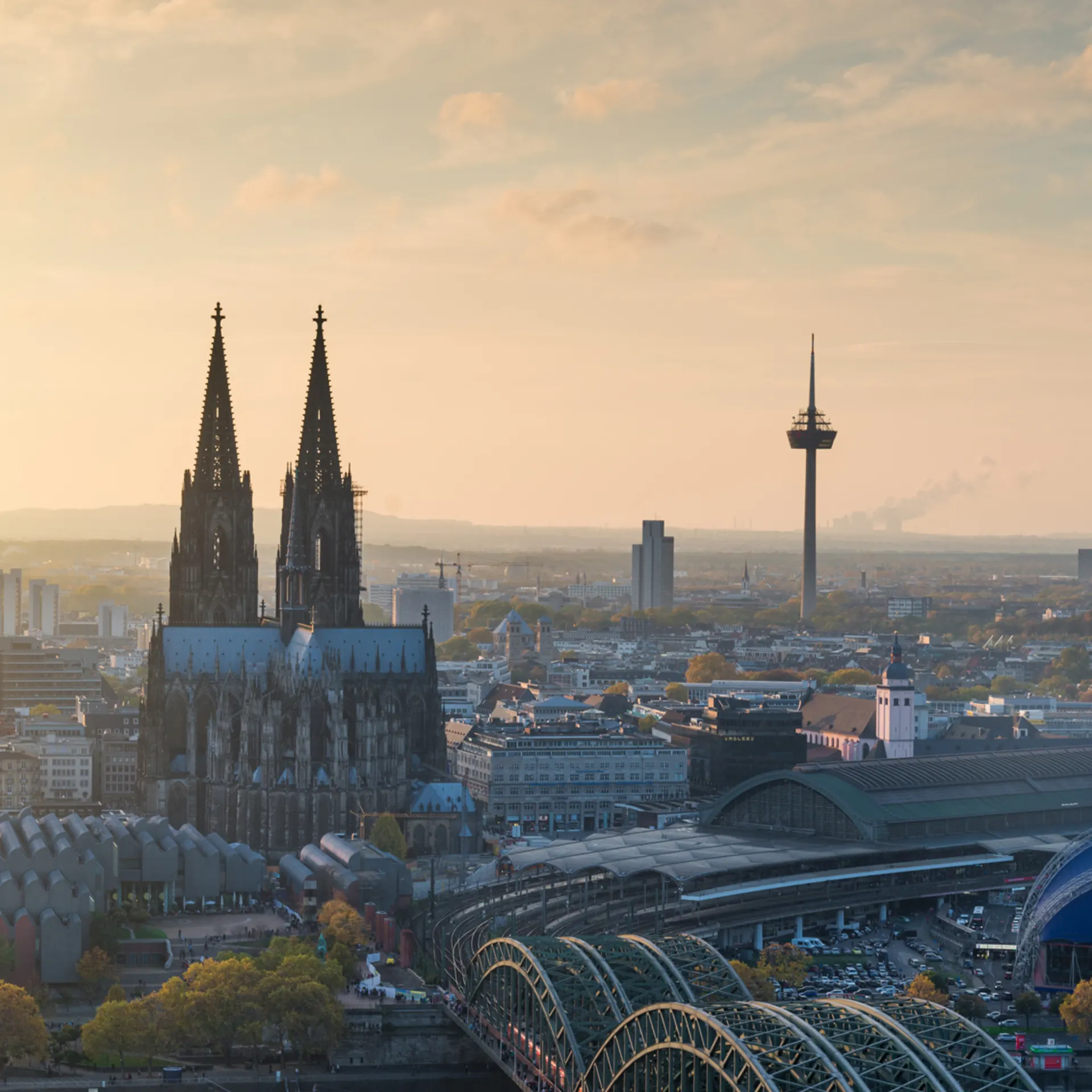 Stadtpanorama mit einem großen Dom, Bahnhof und Brücke bei Sonnenuntergang.