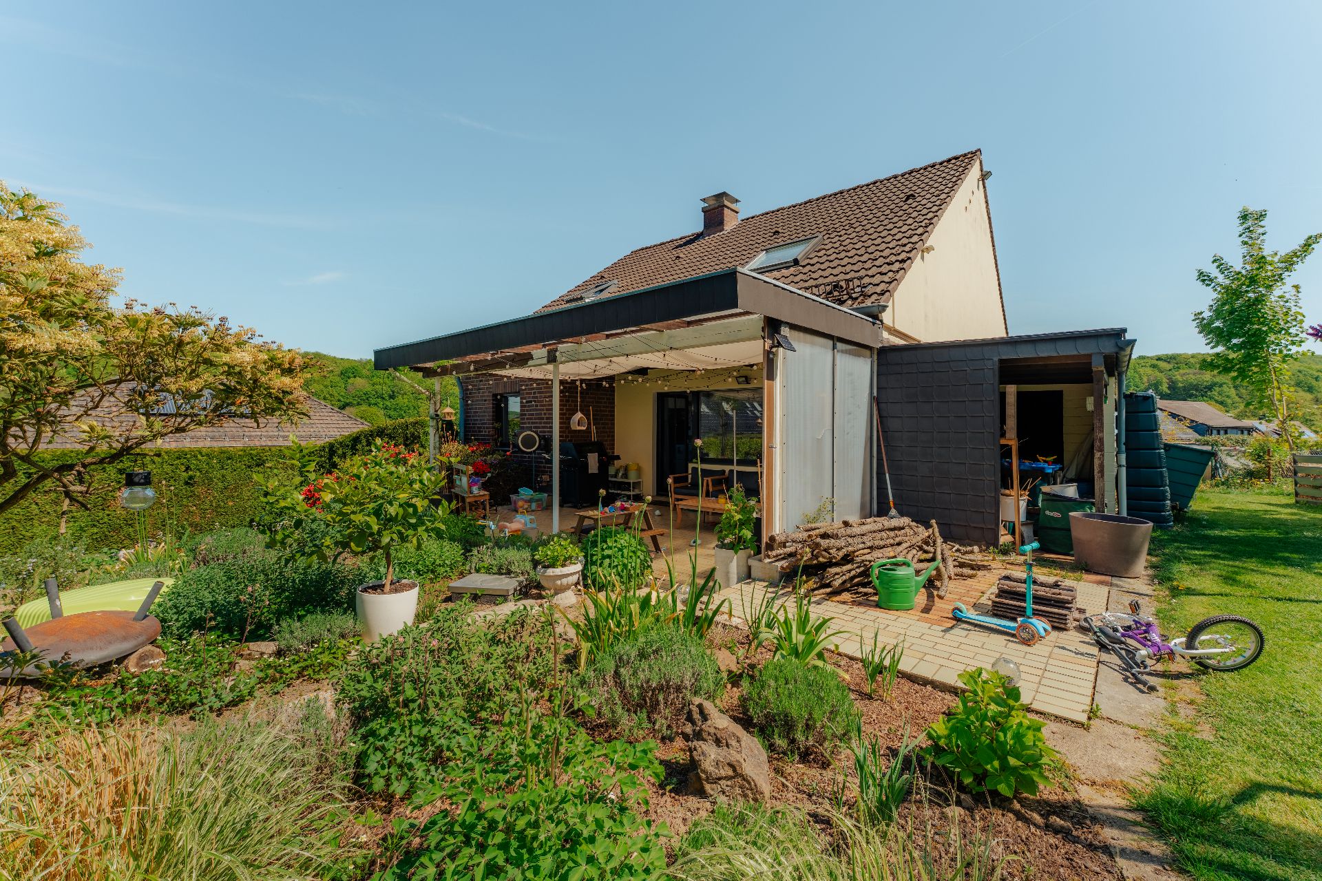Moderner Garten mit Terrasse, Pflanzen, Fahrrädern und einem Einfamilienhaus im Hintergrund.