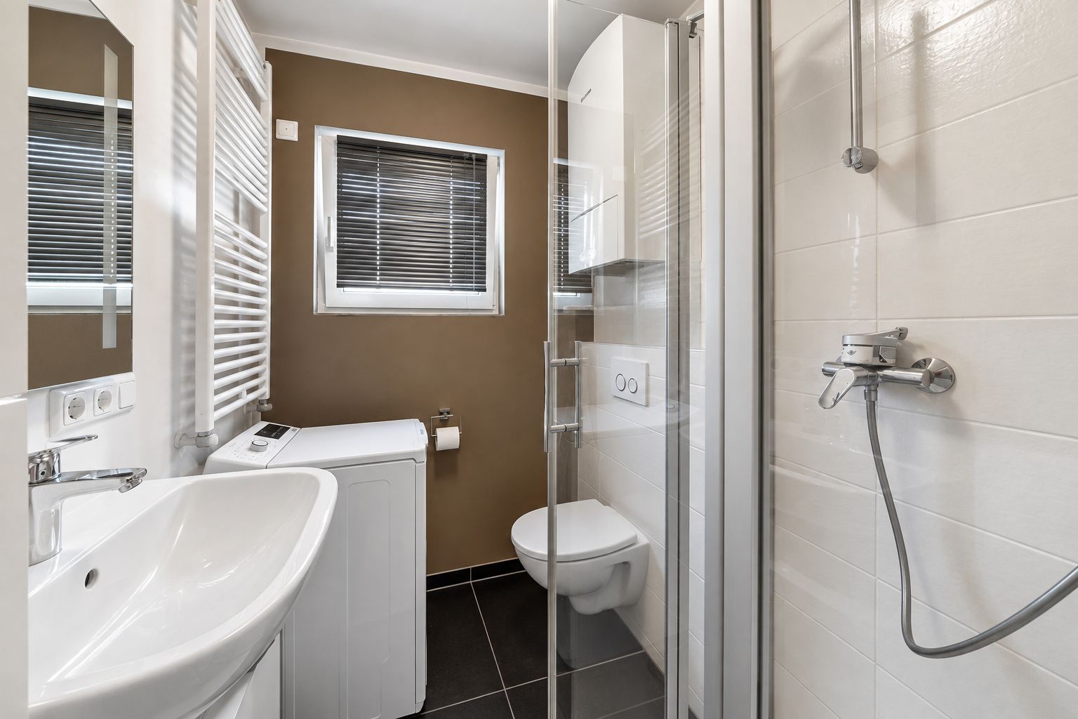 Modernes Badezimmer mit Waschbecken, Waschmaschine, Toilette und Duschkabine.