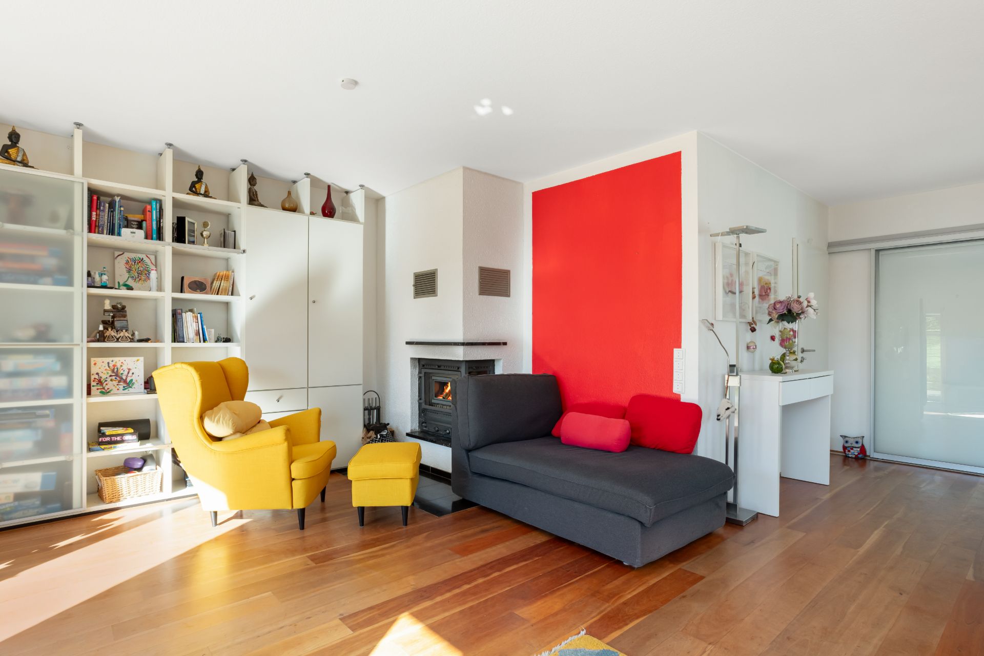 Wohnzimmer mit gelbem Sessel, grauem Sofa, Kamin und Regalwand auf Holzfußboden.