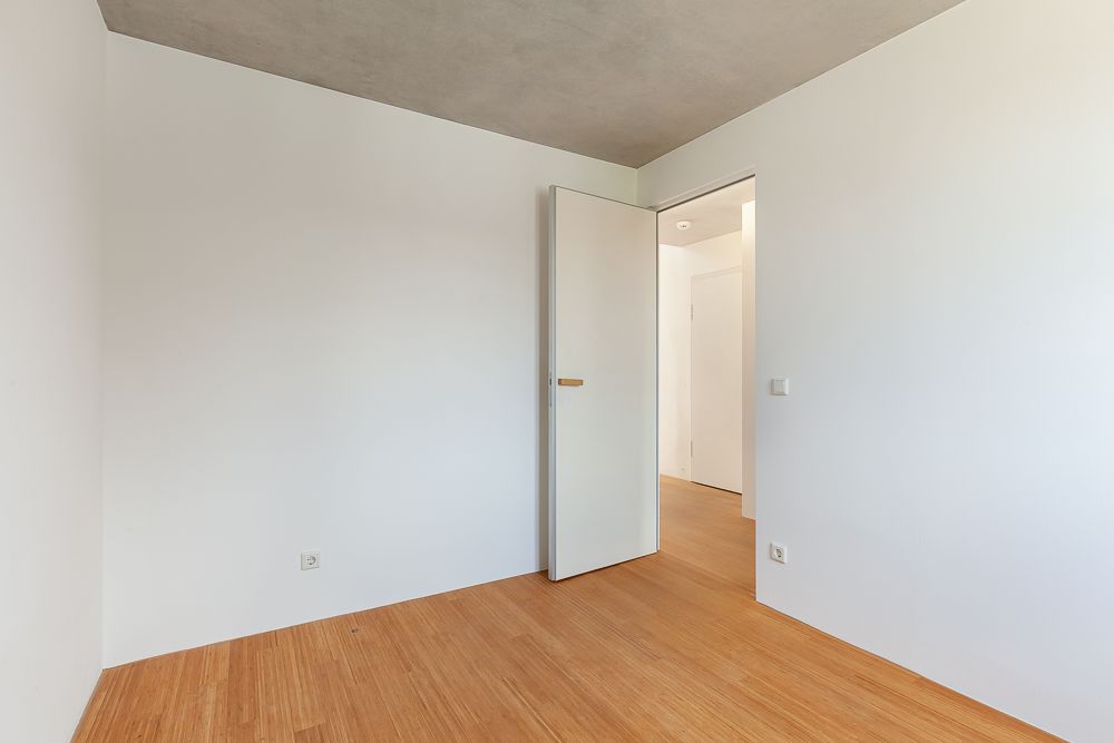 Leerer Raum mit hellem Holzboden, weißen Wänden und offener Tür.