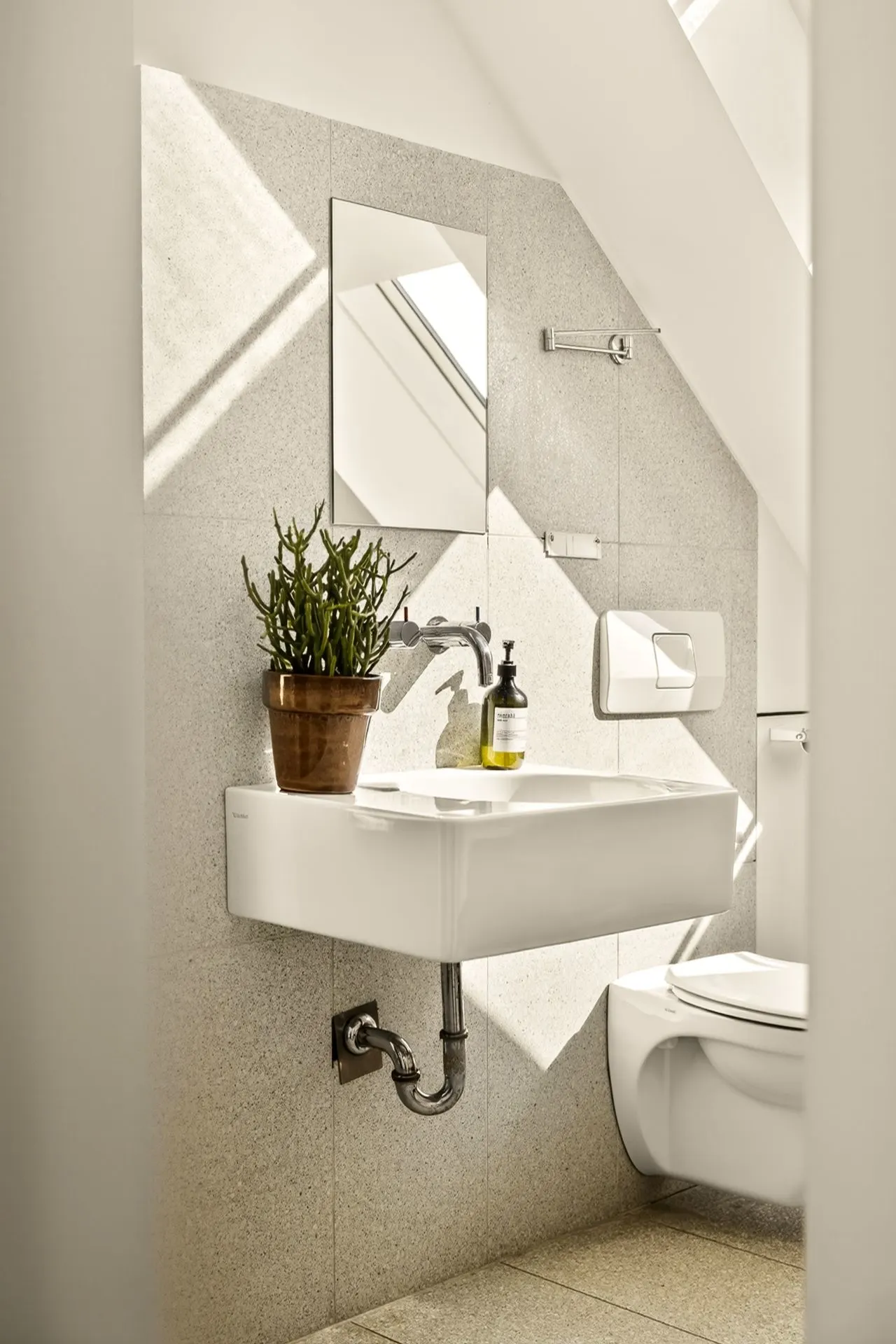 Modernes Bad mit Waschbecken, Spiegel, Pflanze und WC unter Dachschräge.