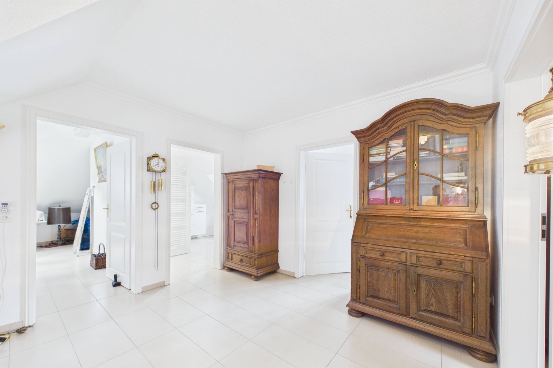 Heller Flur mit Fliesenboden, Holzschrank und Vitrine, mehrere geöffnete Türen zu anderen Zimmern.
