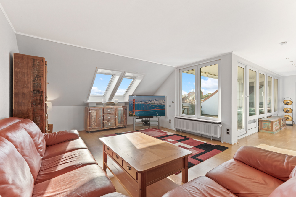 Helles Wohnzimmer mit roten Ledersofas, Holzmöbeln, TV und großen Fenstern.
