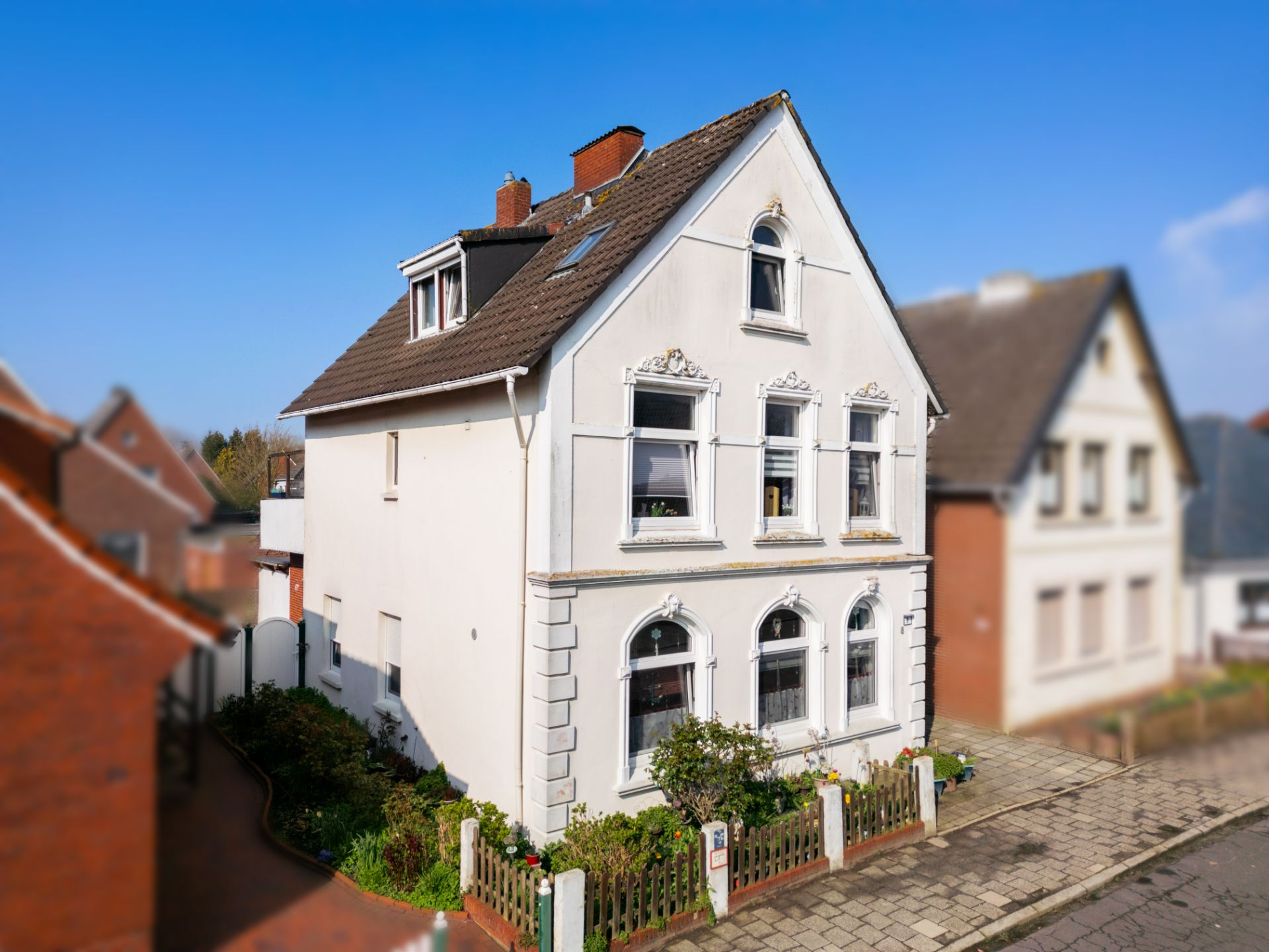 Zweistöckiges, weißes Wohnhaus mit Garten und Dachfenster an einer Straße.