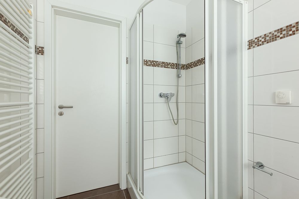 Modernes Bad mit Dusche, weiß gefliesten Wänden und Handtuchheizkörper.