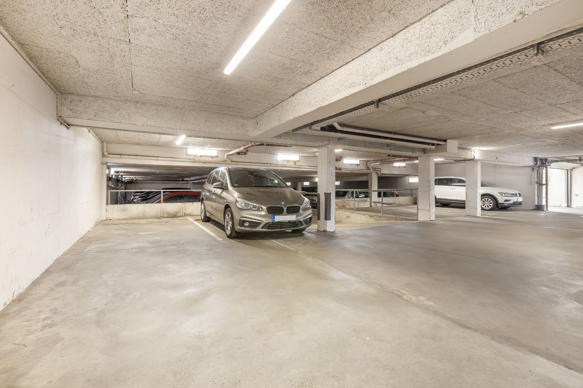 Helle Tiefgarage mit mehreren geparkten Autos auf markierten Parkplätzen.