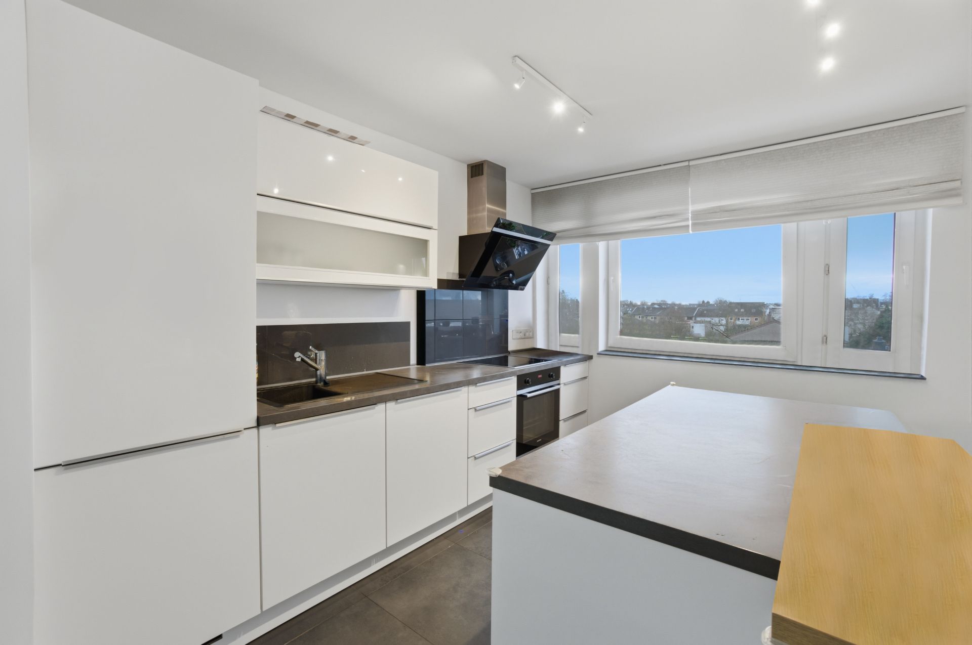 Moderne weiße Einbauküche mit großem Fenster und Blick auf die Stadt.