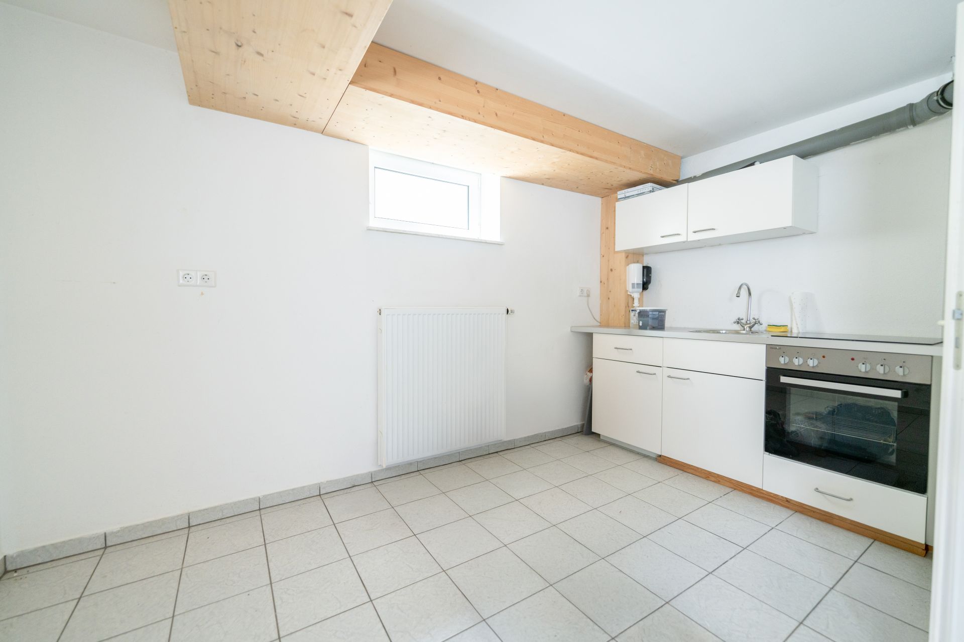Helle Küche mit weißen Schränken, Herd, Fenster und sichtbarem Holzbalken.