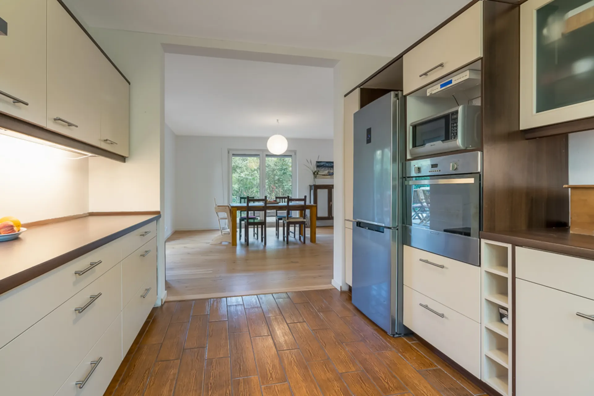 Moderne Küche mit Holzboden und Blick auf ein Esszimmer mit großem Fenster.