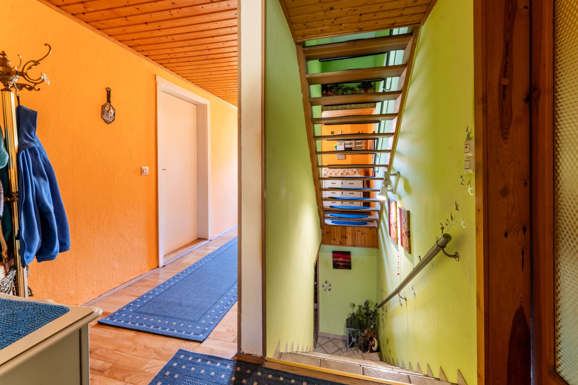 Flur mit Teppichen, Garderobe und offener Treppe mit grün gestrichener Wand.