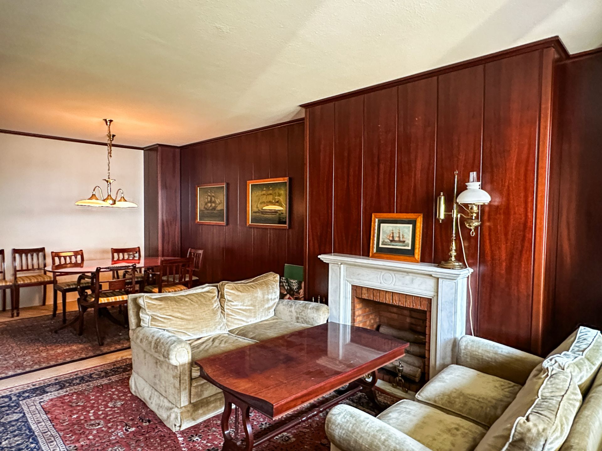 Wohnzimmer mit Kamin, zwei Sofas, Holztisch, Holzwänden und Blick auf Essbereich mit Tisch und Stühlen.