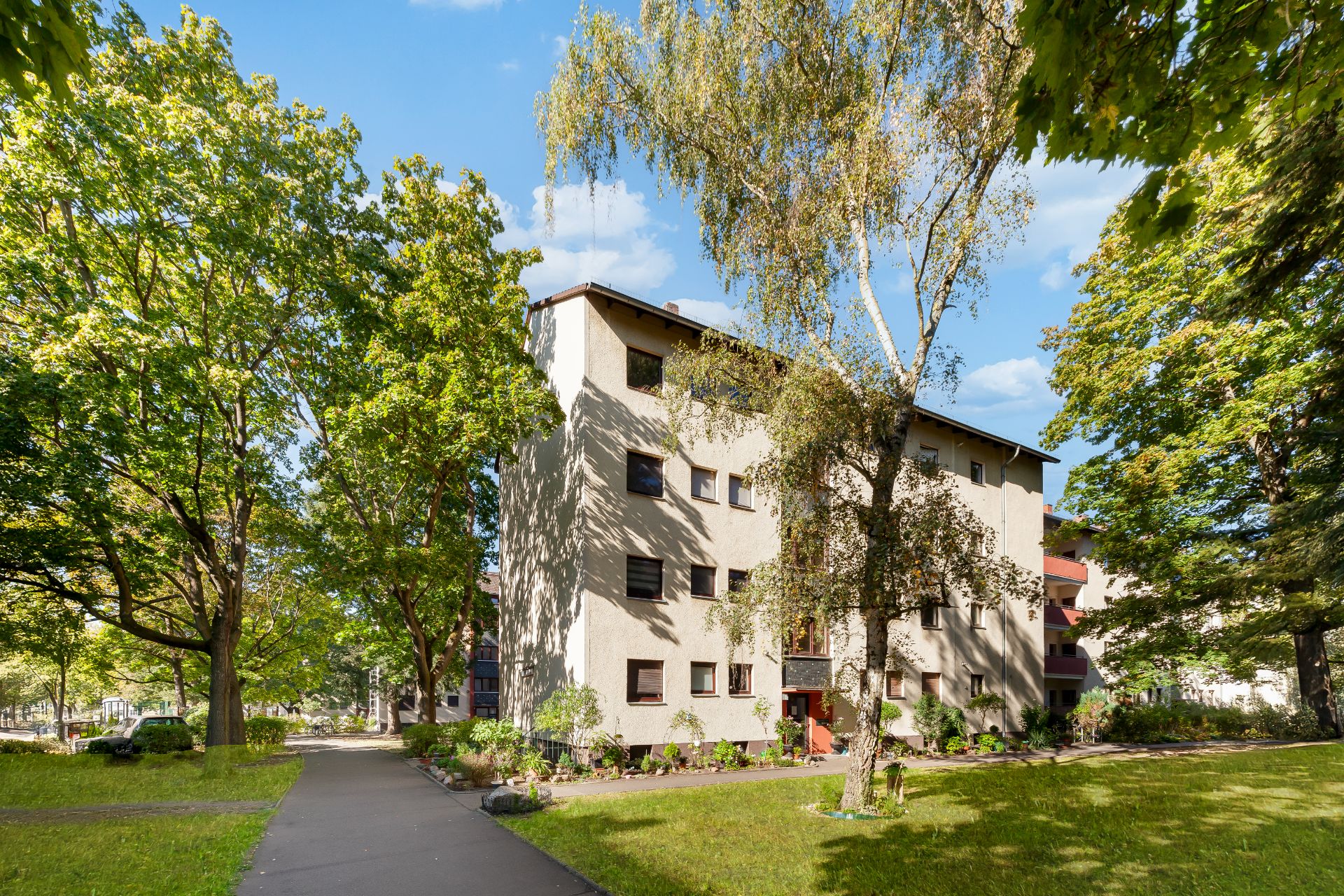 Mehrfamilienhaus mit beigem Putz, umgeben von Bäumen und einer Grünfläche.