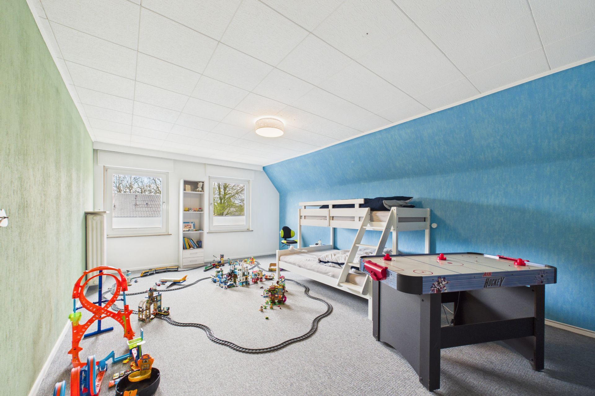 Kinderzimmer mit Hochbett, Spielzeug, großem Fenster und Airhockey-Tisch.