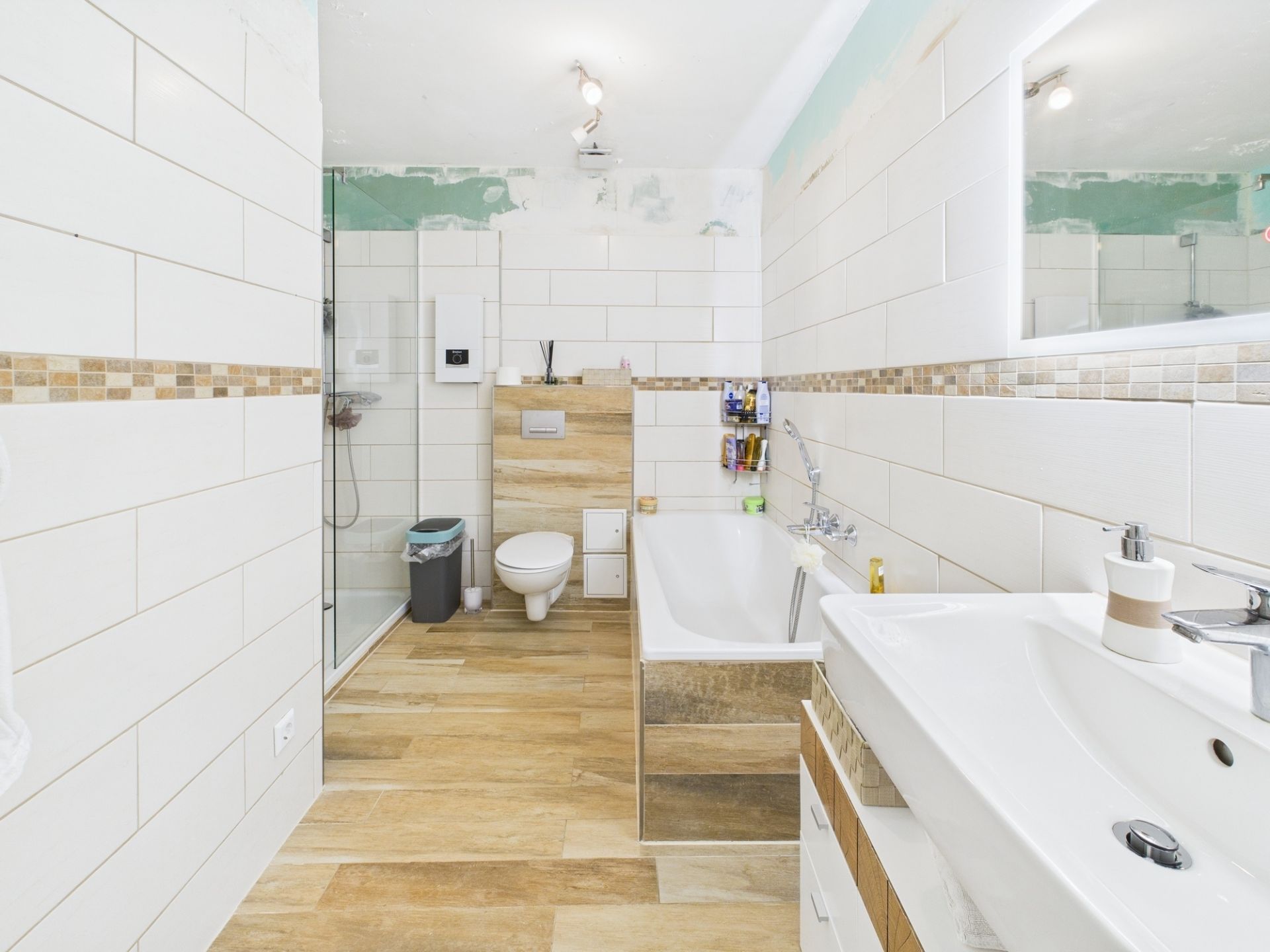 Modernes Badezimmer mit Dusche, Badewanne, WC und Waschbecken, helle Fliesen und Holzboden.