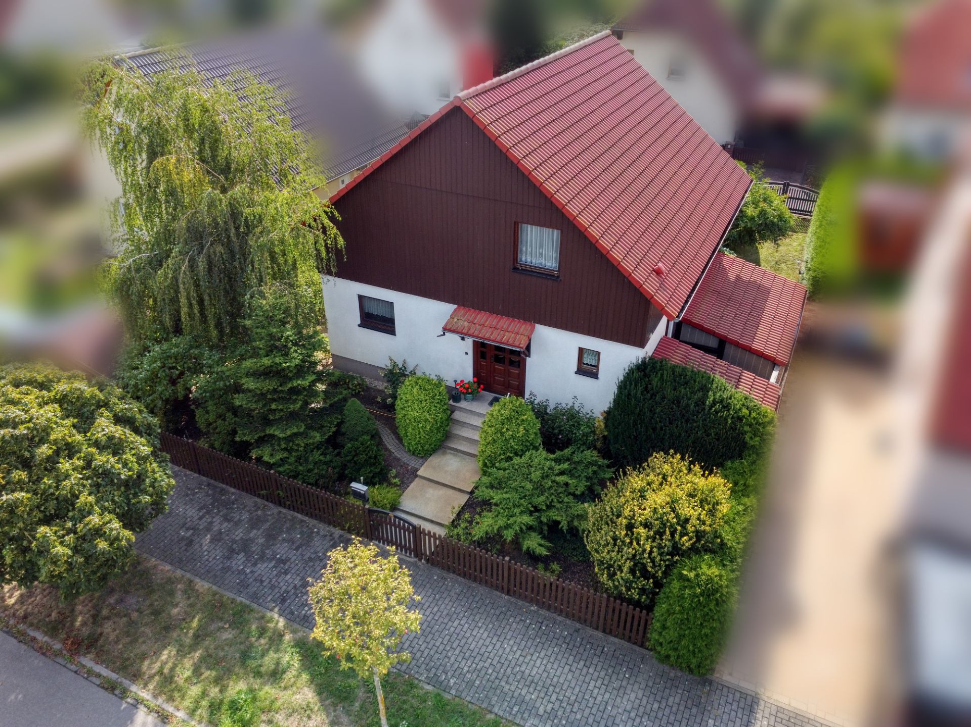 Einfamilienhaus mit rotem Dach, Vorgarten und umlaufendem Zaun aus der Vogelperspektive.
