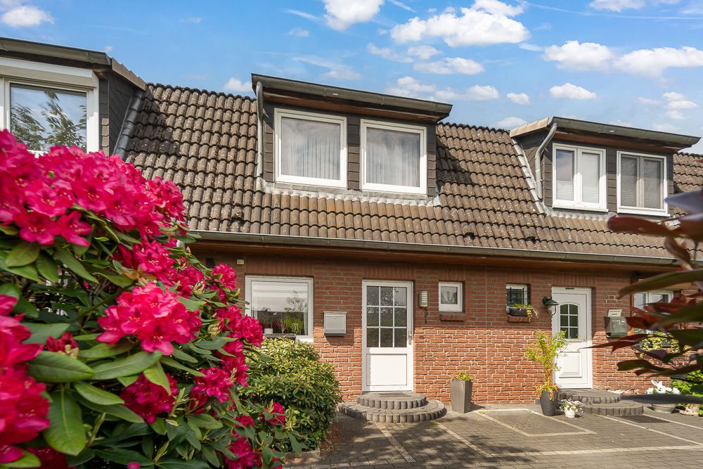 Reihenhaus mit rotem Ziegelstein, braunem Dach und Blumen im Vordergrund.