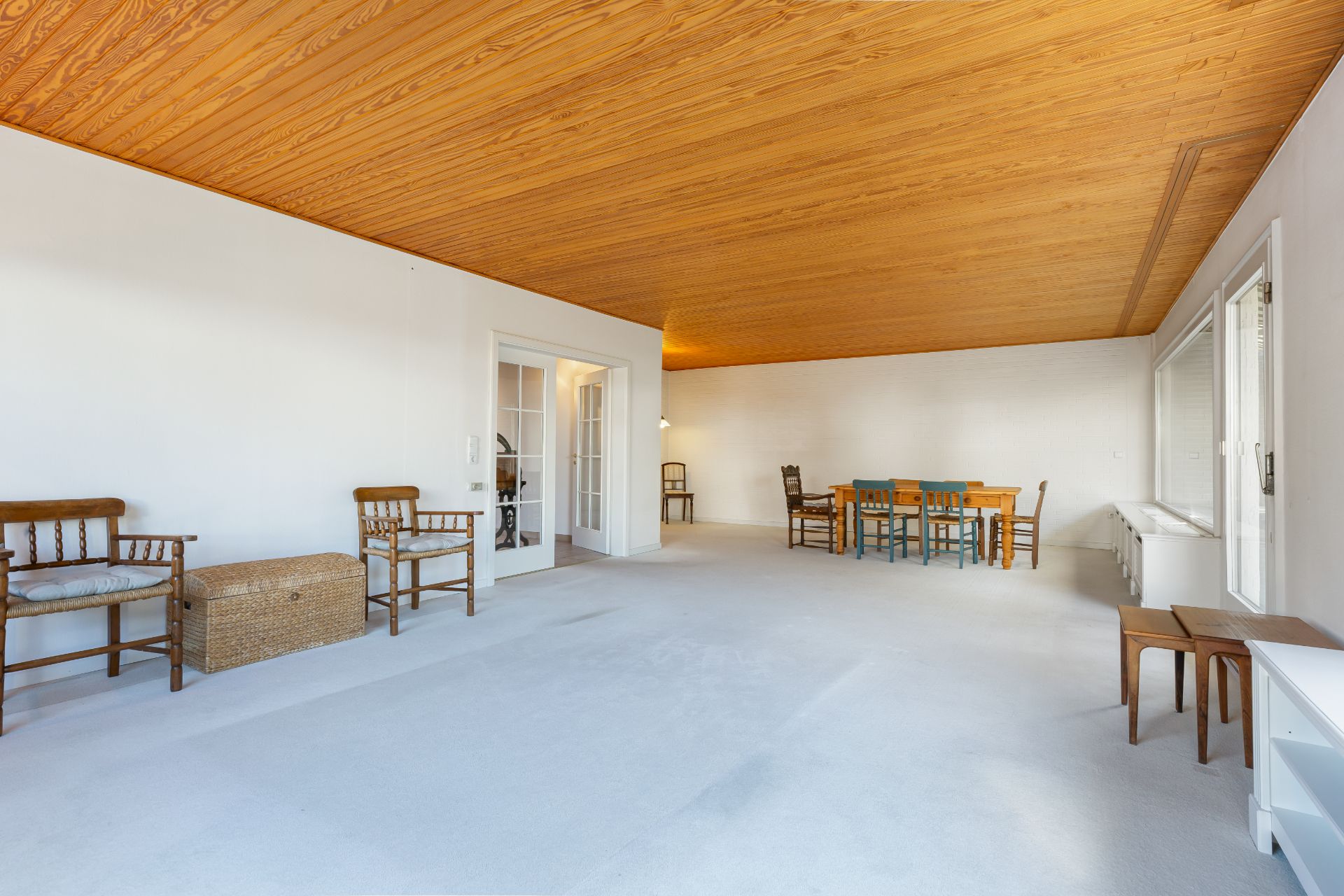 Großes Wohnzimmer mit Holzbalkendecke, mehreren Stühlen, einem Esstisch und weißen Wänden.