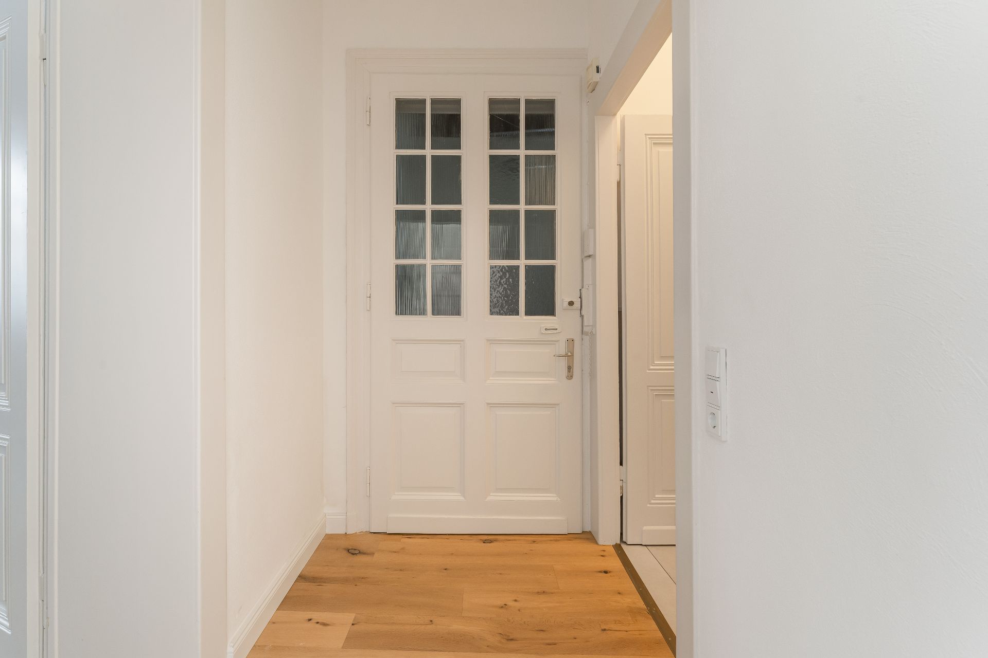 Heller Flur mit Holzboden und weißer Tür mit Glasfenstern.