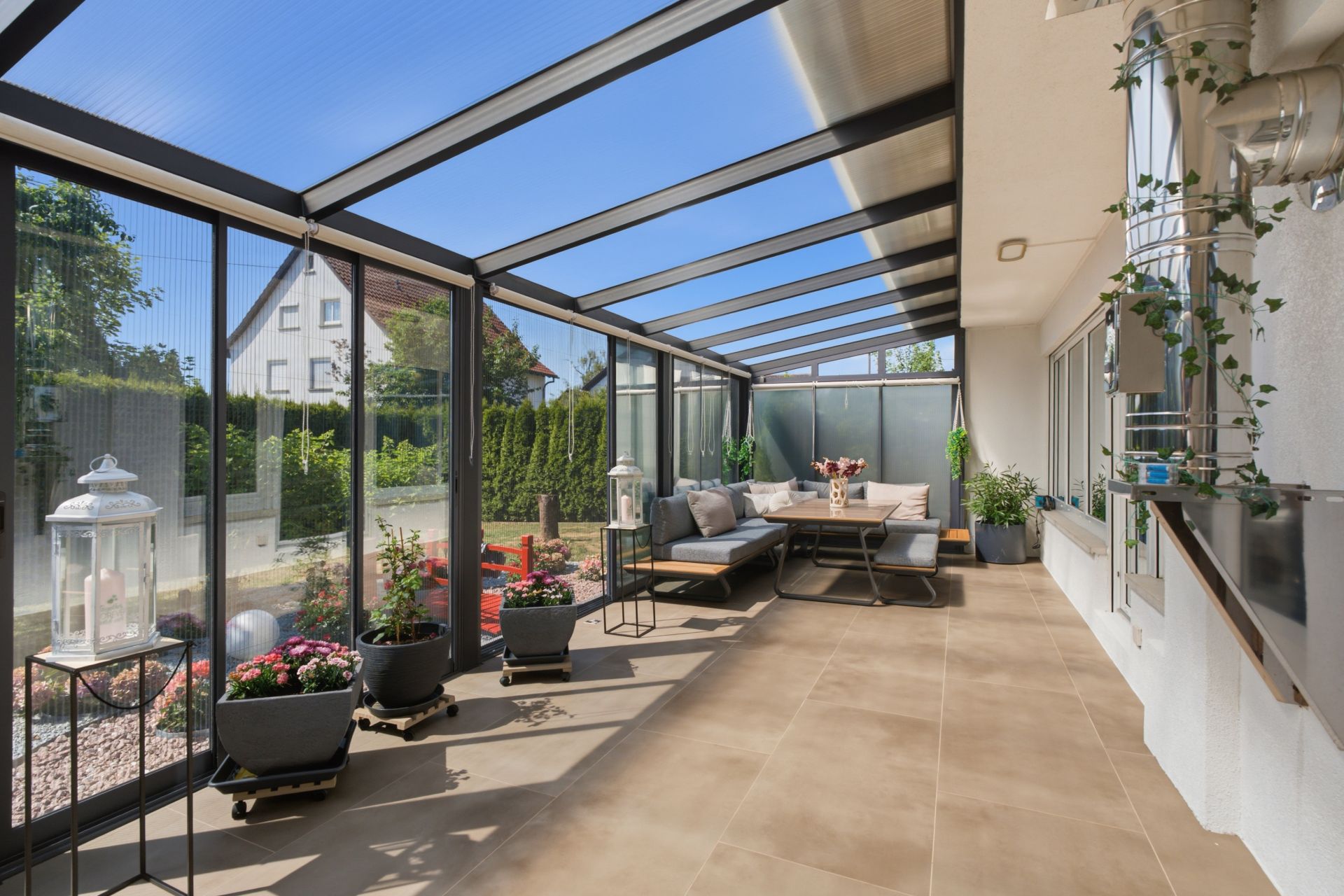 Wintergarten mit Glasdach, Sitzgruppe, Pflanzen und Blick in den Garten.