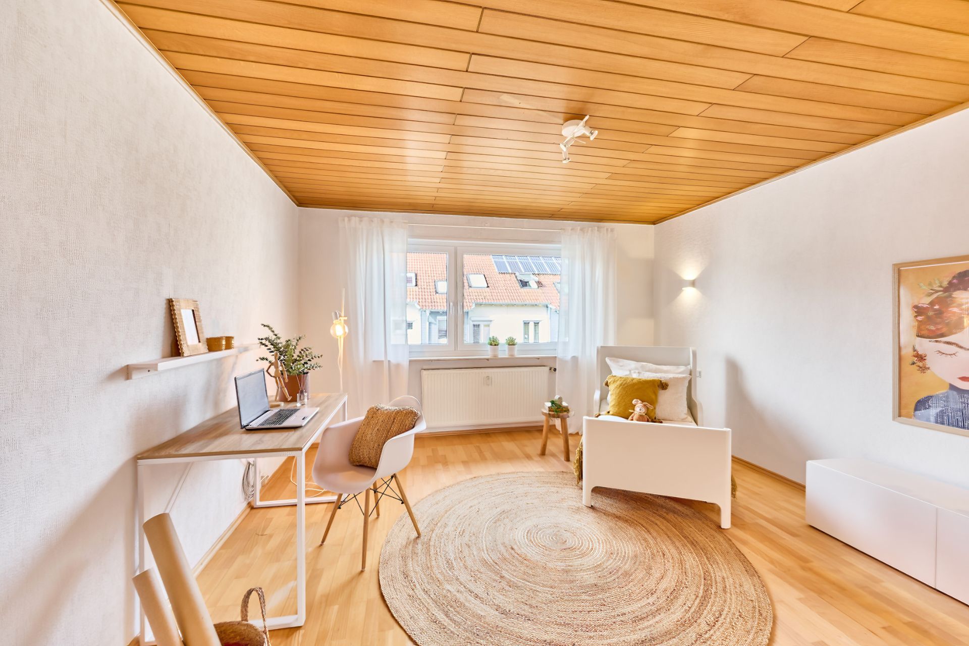 Helles Wohnzimmer mit Schreibtisch, Sessel, Teppich und großem Fenster.