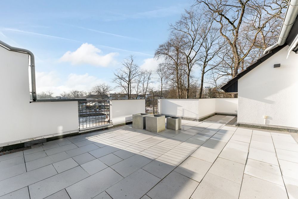 Große Dachterrasse mit Fliesenboden und drei Sitzmöbeln, umgeben von weißen Wänden.