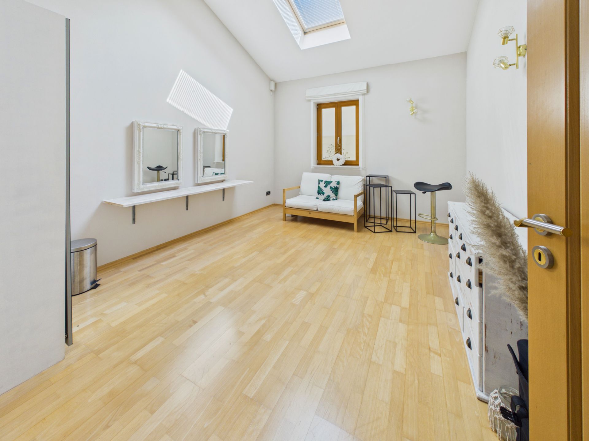 Heller Raum mit Holzfußboden, Sofa, Spiegeln, Fenster und dekorativem Tisch.