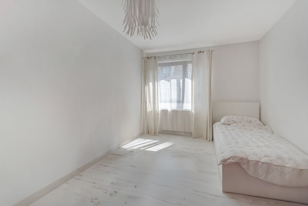 Helles, schmales Schlafzimmer mit Einzelbett, Fenster und weißen Vorhängen.
