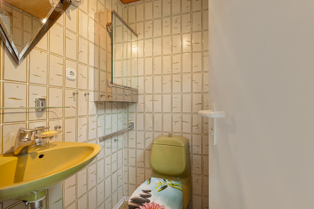 Kleines Badezimmer mit gelbem Waschbecken, Toilette und gemusterten Fliesen.