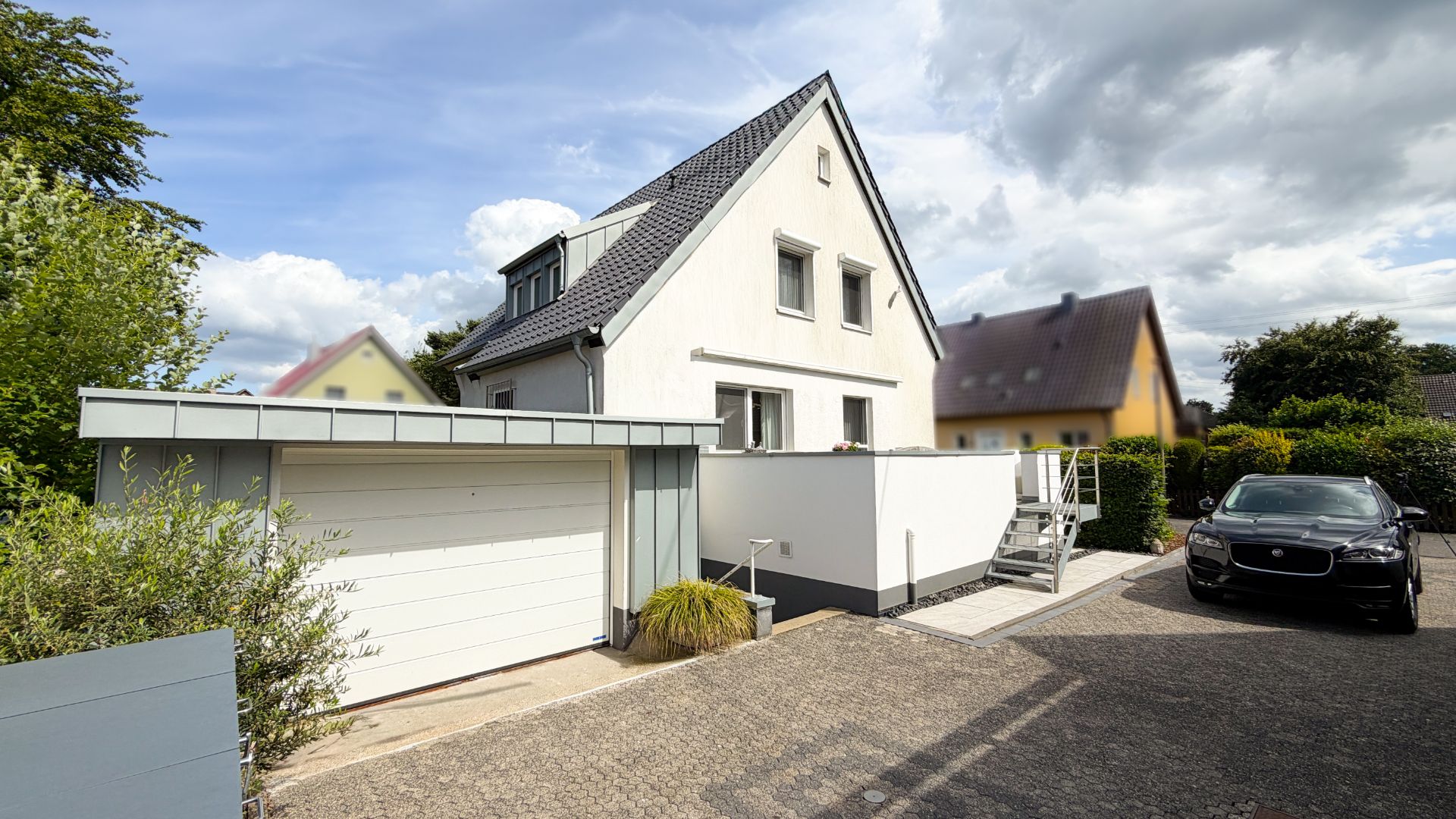 Modernes Einfamilienhaus mit Garage, Auto und kleiner Treppe im Vorgarten.