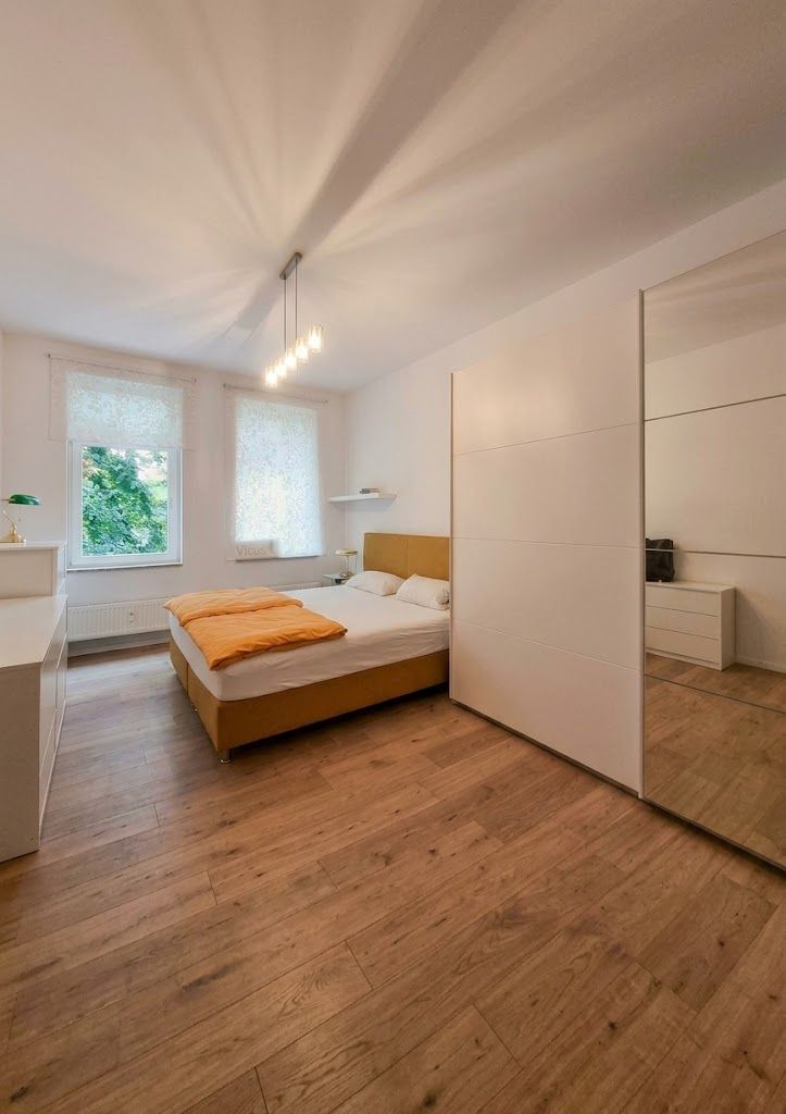 Helles Schlafzimmer mit Doppelbett, großem weißen Kleiderschrank und Holzboden.
