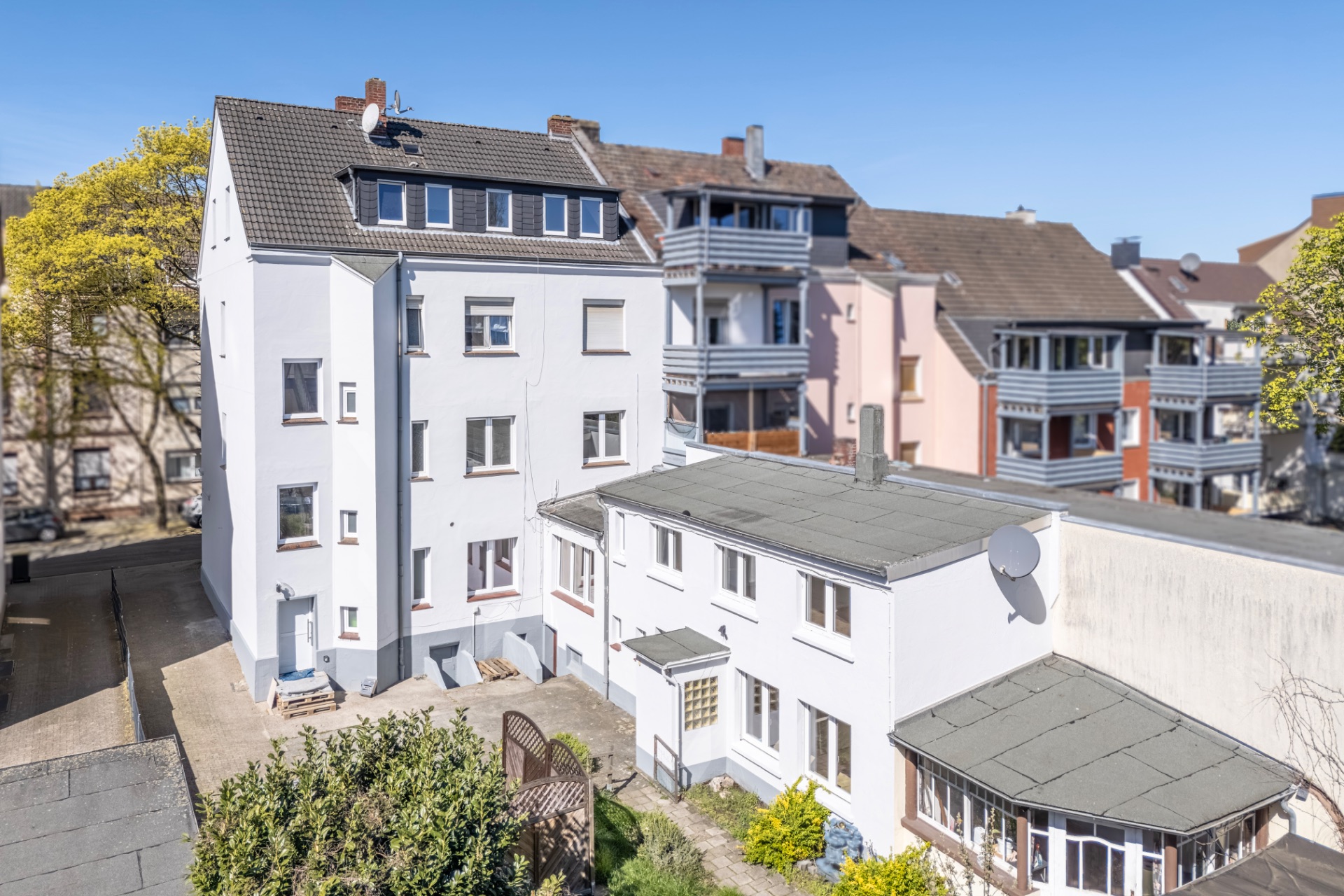 Mehrfamilienhaus mit Nebengebäude und kleinem Innenhof, umgeben von weiteren Wohnhäusern.