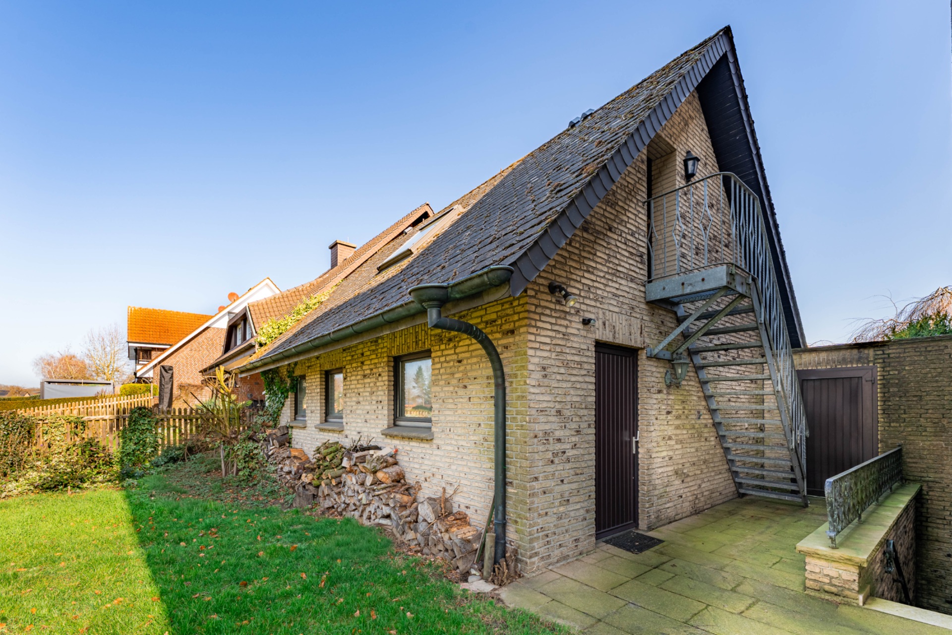 Backstein-Wohnhaus mit Dachschrägen, Außentreppe und Garten.