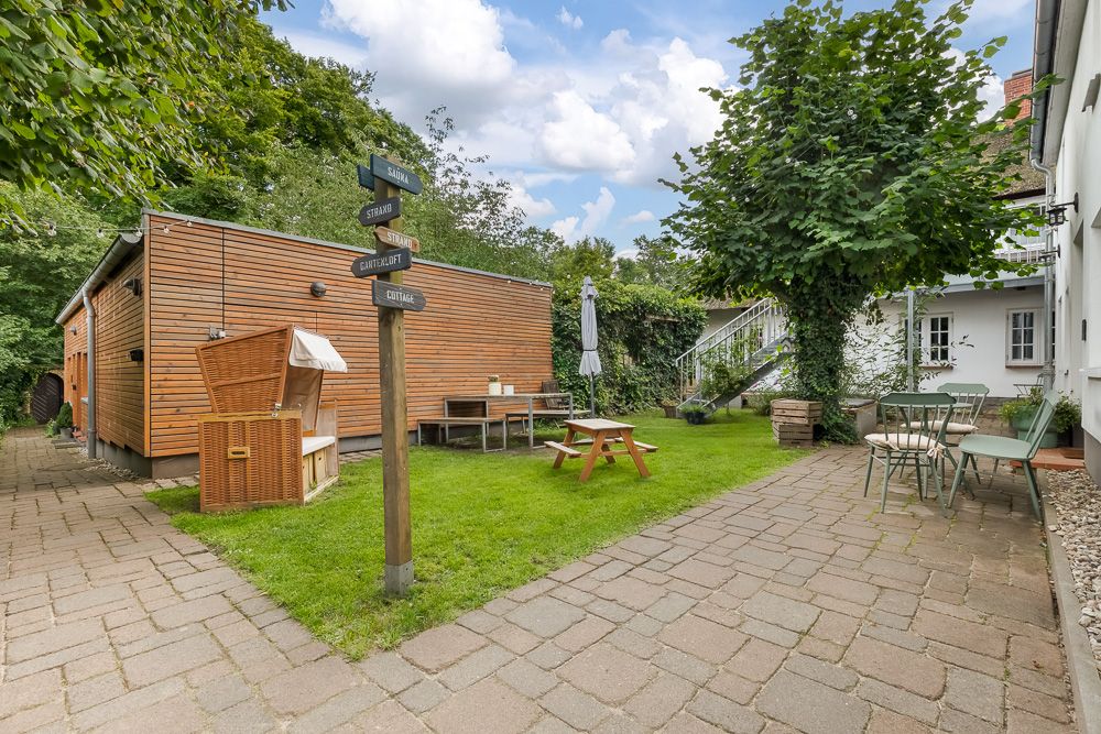 Gepflegter Garten mit Sitzmöbeln, Holzhaus, Wegweiser und Bäumen bei einem Wohnhaus.