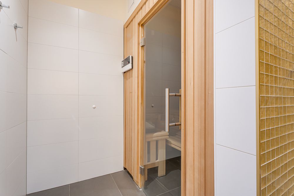 Heller Raum mit moderner Holztür zur Sauna und weißen Fliesen an den Wänden.