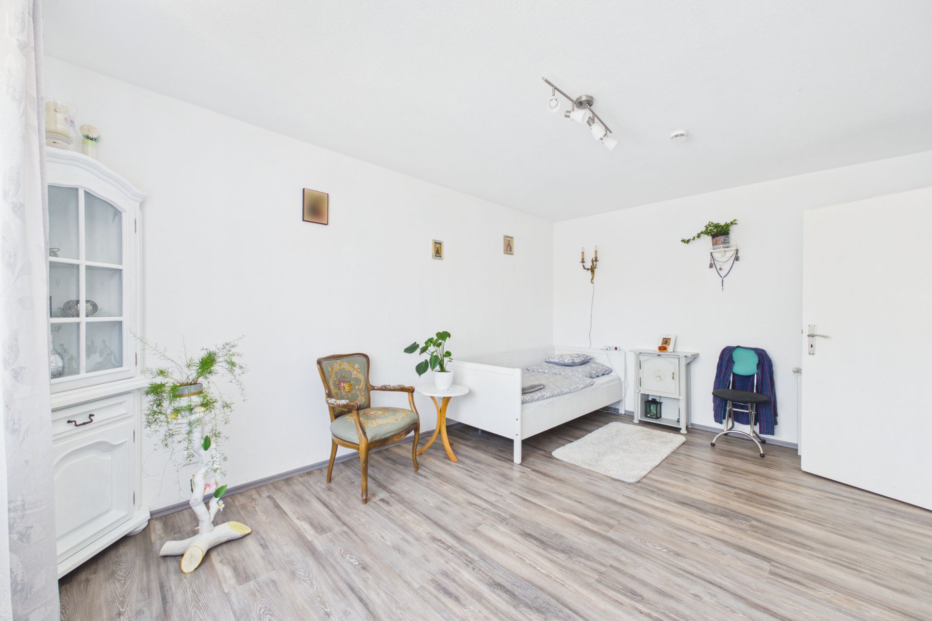 Helles Zimmer mit Einzelbett, Sessel, Schreibtisch und Holzfußboden.