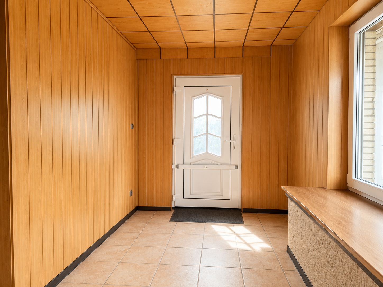 Flur mit hellen Holzvertäfelungen, weißer Haustür und großem Fenster.