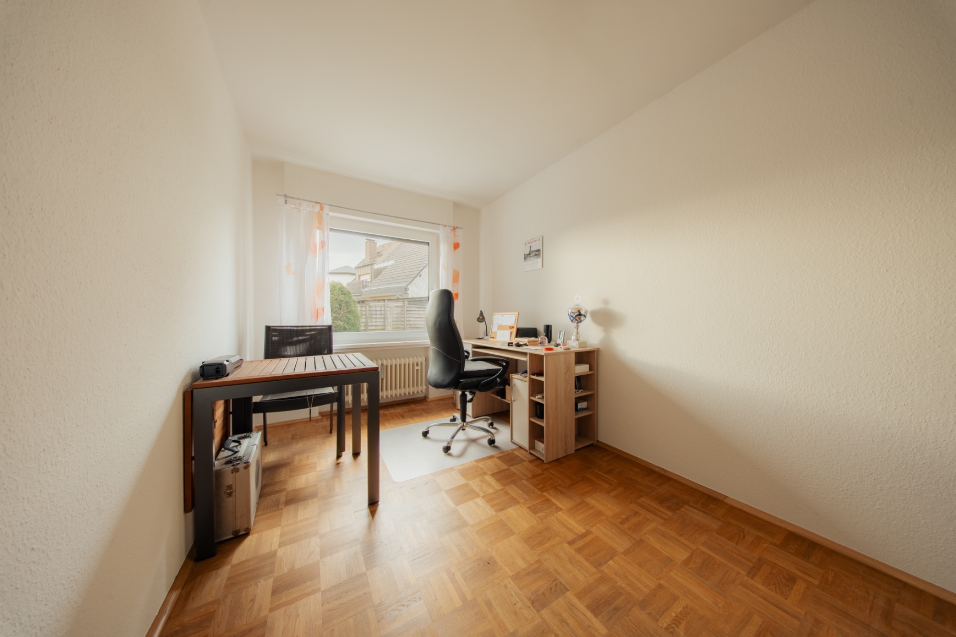 Helles Arbeitszimmer mit zwei Schreibtischen, Stuhl, Holzfußboden und großem Fenster.