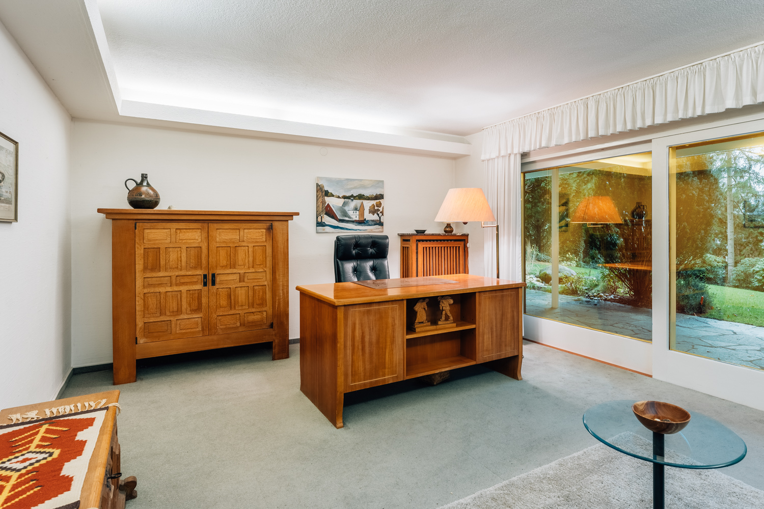 Helles Arbeitszimmer mit Holzmöbeln, Schreibtisch und großem Fenster mit Blick in den Garten.
