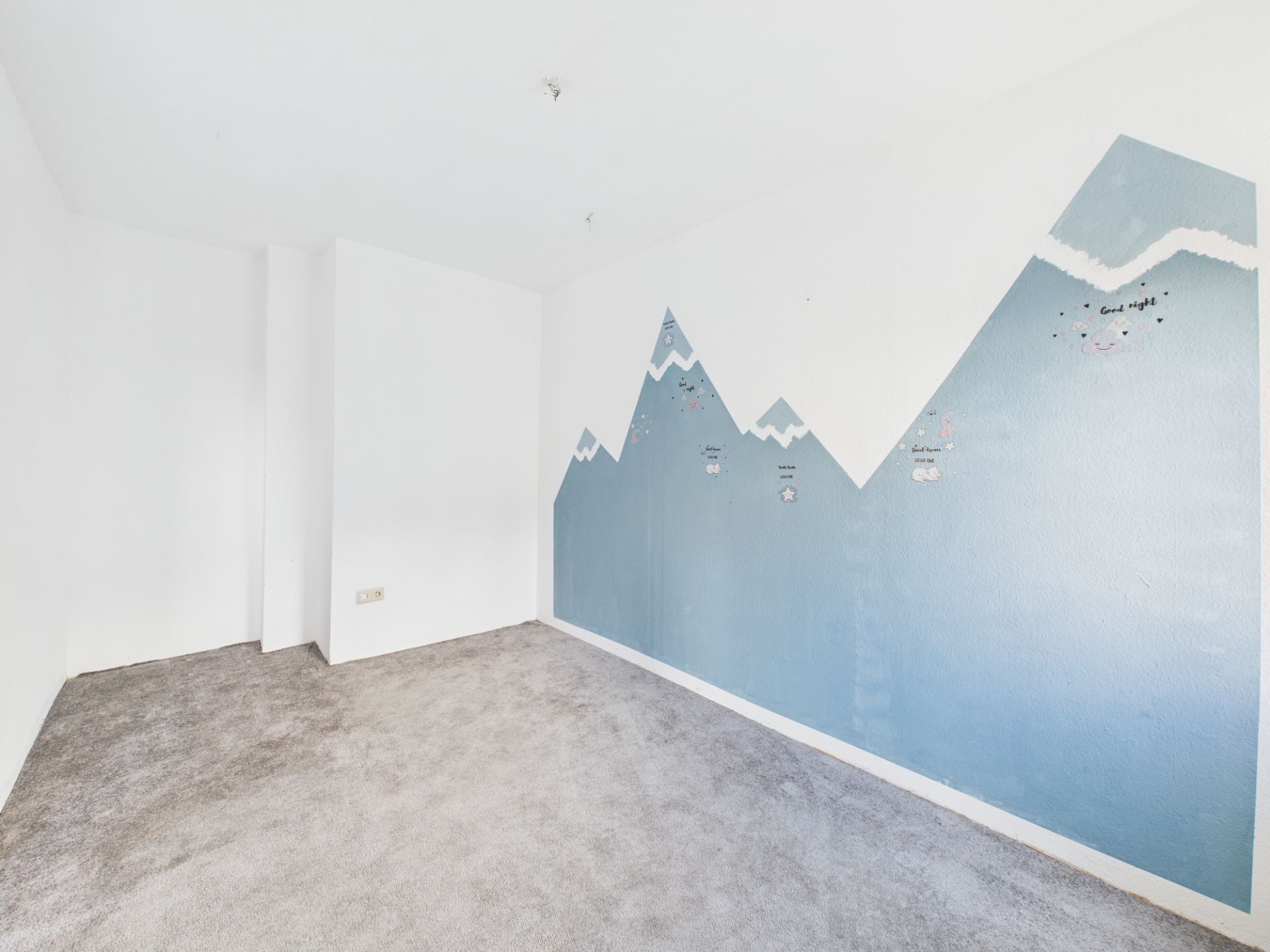 Leeres Zimmer mit Teppichboden und gemalter Berglandschaft an der Wand.
