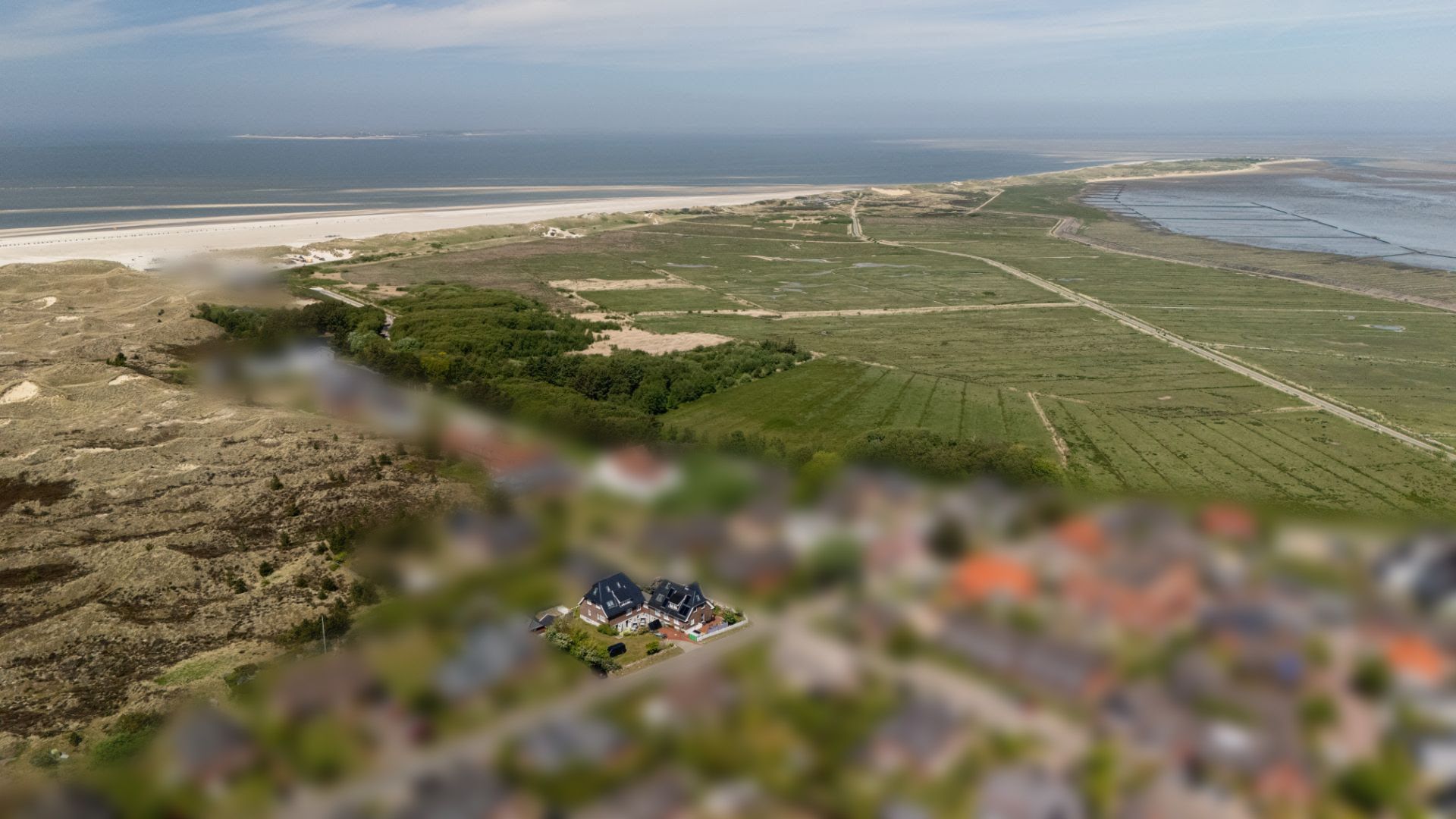 Luftaufnahme von Häusern nahe Strand, umgeben von Dünen, Wiesen und Meer.