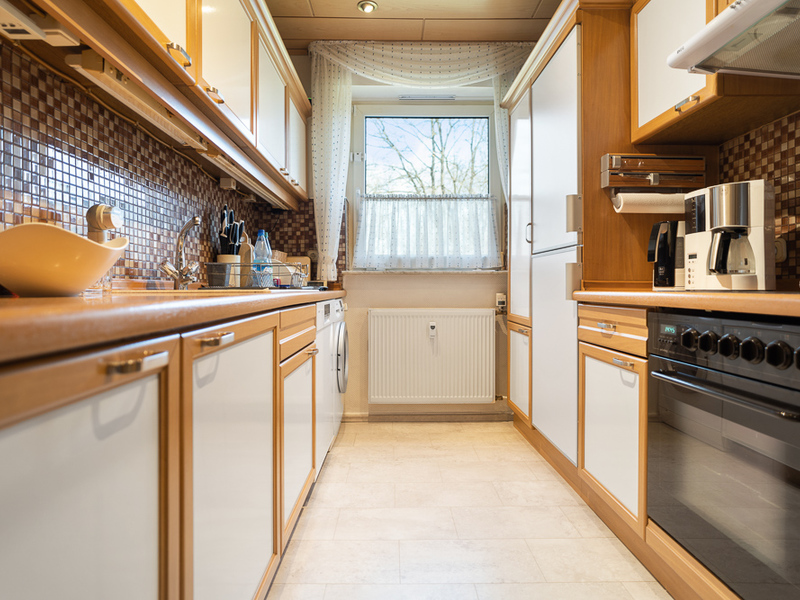 Helle Küche mit Holzmöbeln, weißen Fronten, Fenster und modernen Geräten.