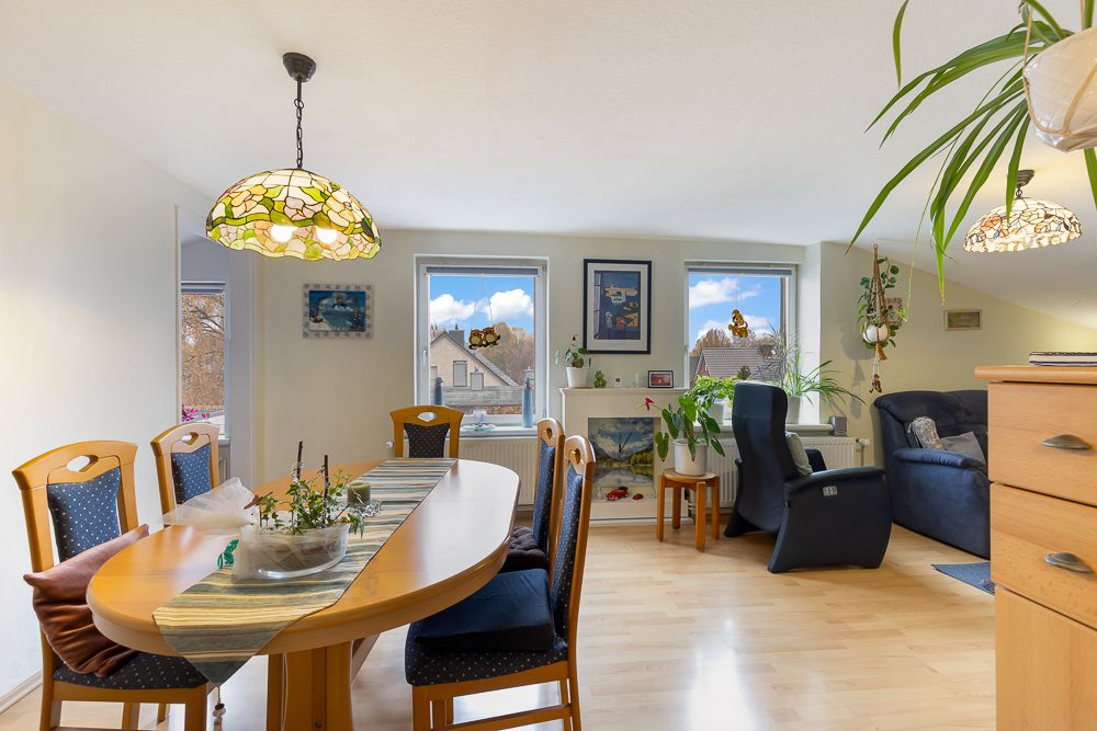 Helles Wohnzimmer mit Esstisch, Stühlen, Sofa, Pflanzen und großen Fenstern.