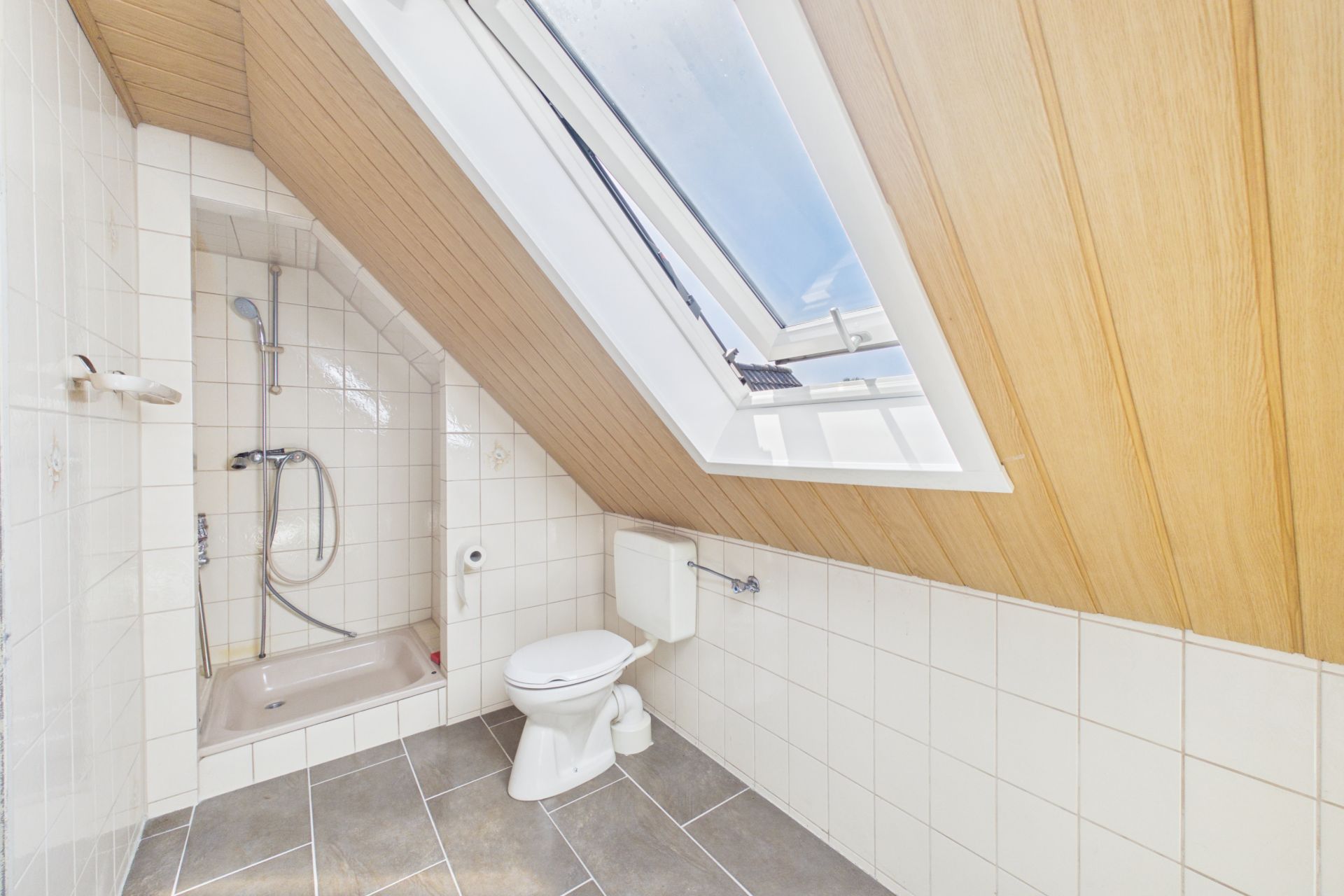 Bad mit Dusche, WC und Dachfenster unter einer schrägen Holzdecke.