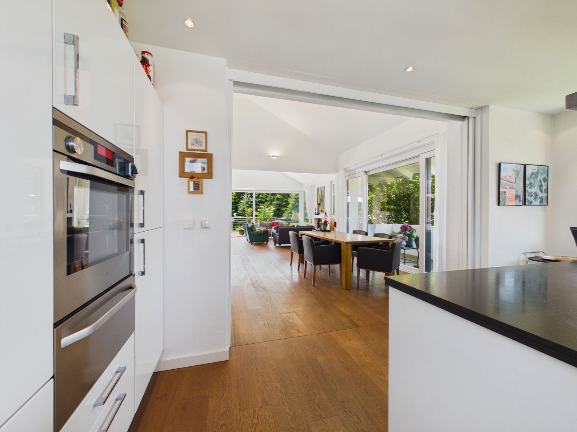 Helle Küche mit Blick auf Esszimmer und Wohnzimmer mit Holzboden und großen Fenstern.